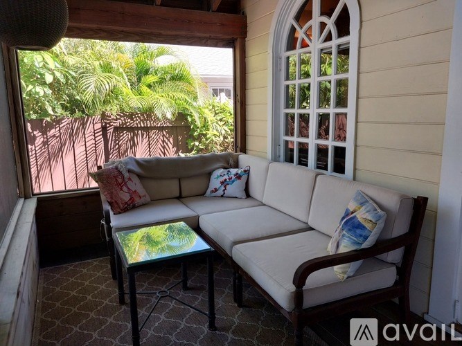 A white couch with a glass table in front of a window with a view of greenery outside.