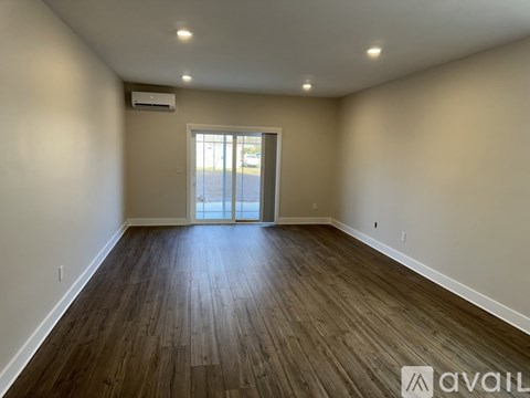 A spacious room with wooden flooring and a sliding glass door.