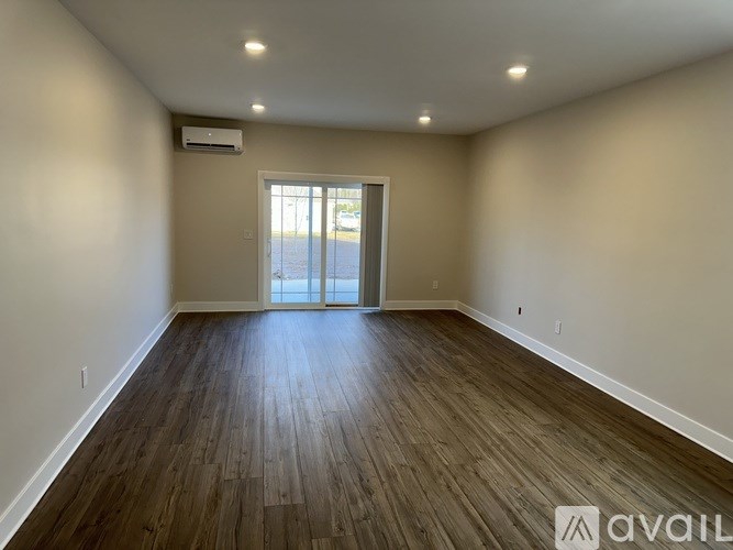 A spacious room with wooden flooring and a sliding glass door.