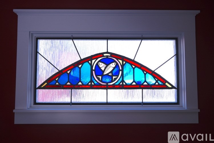 A stained glass window in a white frame with a blue and red design.