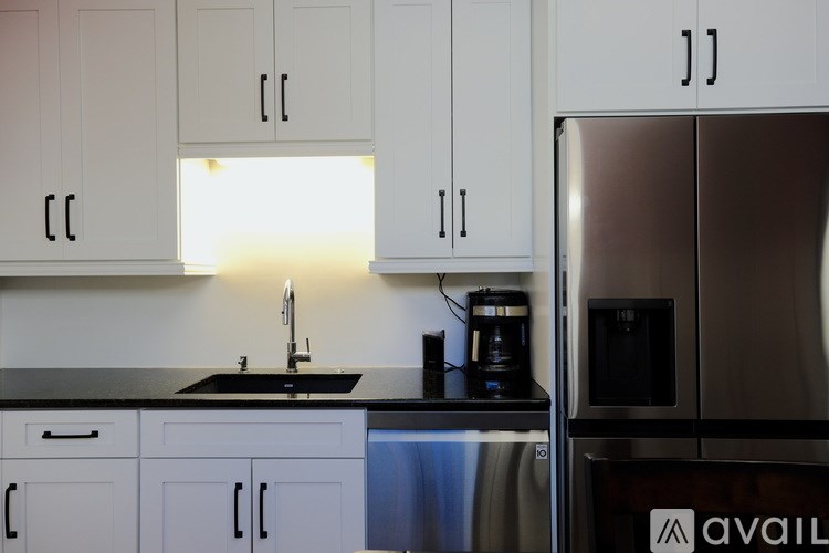 A kitchen with white cabinets and a black countertop with a sink and a coffee maker.