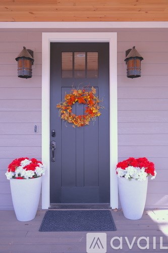 A grey door with a wreath and two pots of flowers on the porch.