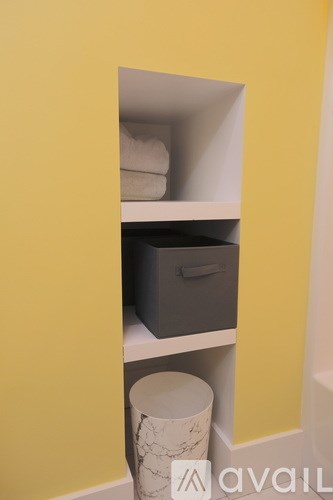 A white container is on the shelf of a yellow wall.