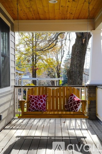 A wooden bench with a red and white pillow sits on a wooden porch.