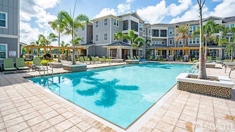 A large swimming pool surrounded by a tiled patio and lounge chairs.