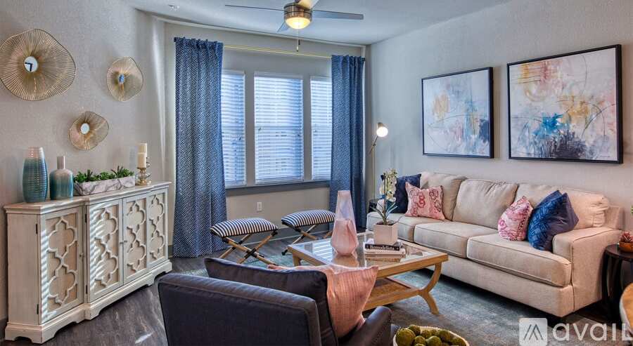 A living room with a white sofa, a wooden coffee table, and a large window with blue curtains.