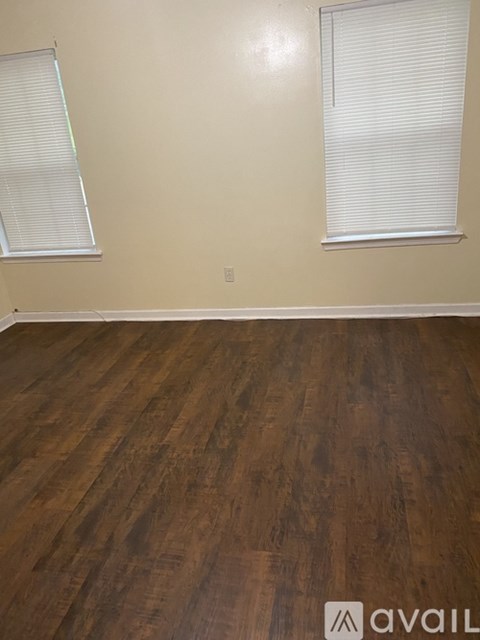 A room with wooden flooring and two windows with blinds.