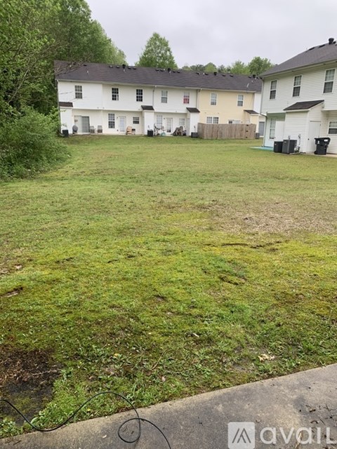A grassy area in front of a white house with a black roof.