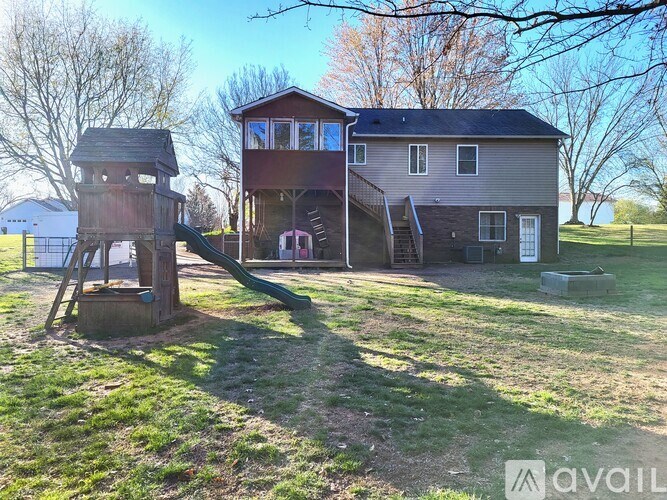 A playground with a slide and a treehouse in front of a house.