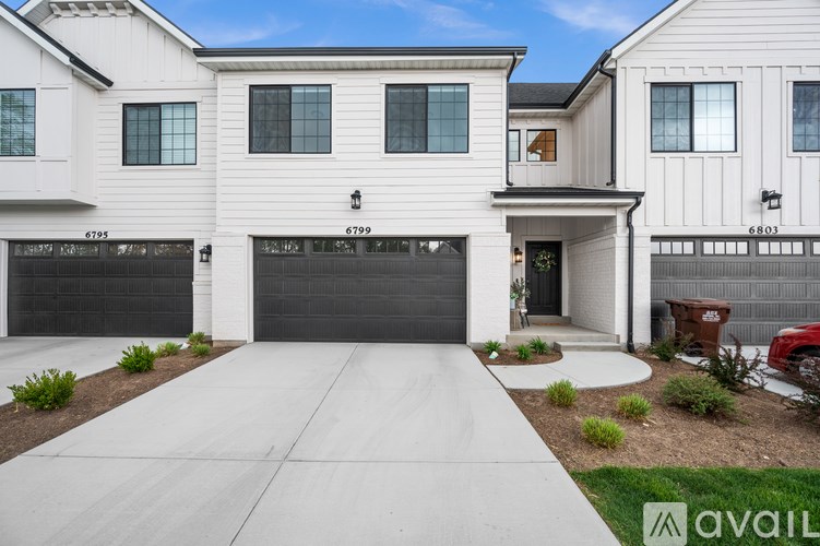 A white house with a black garage door is numbered 6799.