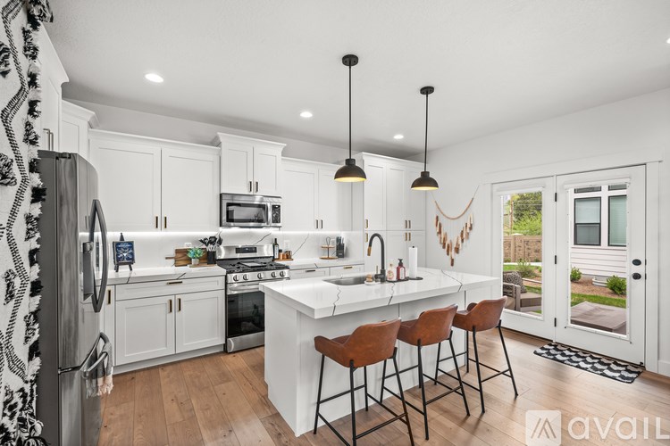 A kitchen with white cabinets and a white island with brown chairs.