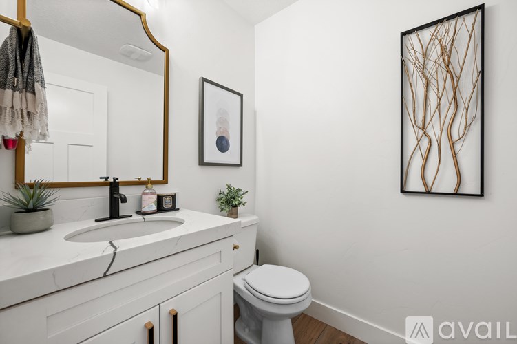 A bathroom with a white toilet, a sink with a mirror above it, and a framed picture on the wall.