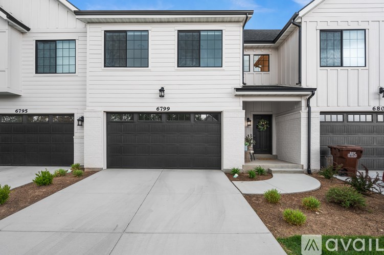 A modern house with a large driveway and a garage door that is open.