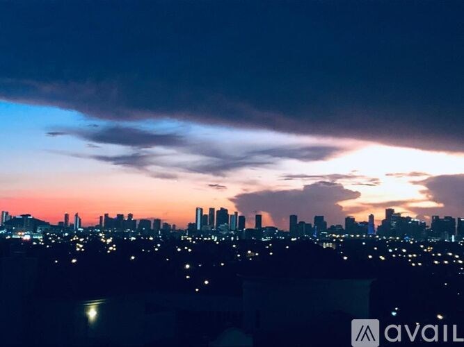 A city skyline at dusk with buildings illuminated against a darkening sky.