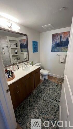 A bathroom with a toilet, sink, and a painting on the wall.