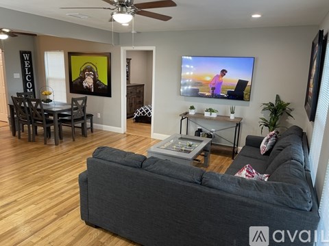 A living room with a grey couch, a dining table with chairs, a television, and a ceiling fan.