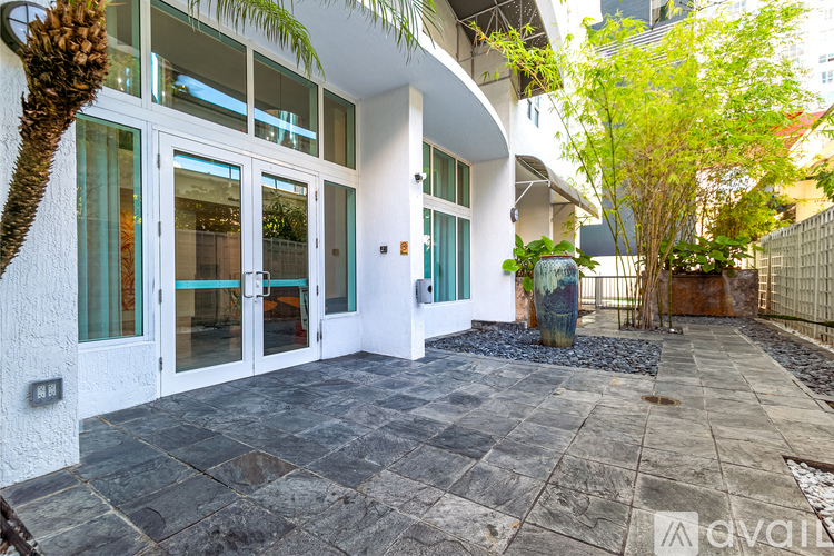 A white building with glass doors and windows is surrounded by a stone patio and a fence.