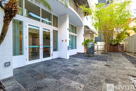 A white building with glass doors and windows is surrounded by a stone patio and a fence.