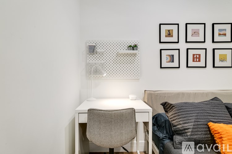 A white desk with a chair and a couch with pillows in front of a wall with pictures on it.