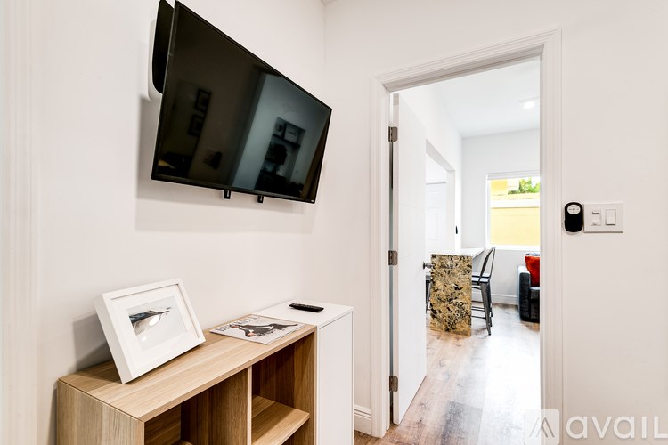 A black television is mounted on a white wall above a wooden stand with a picture frame and a magazine on it.