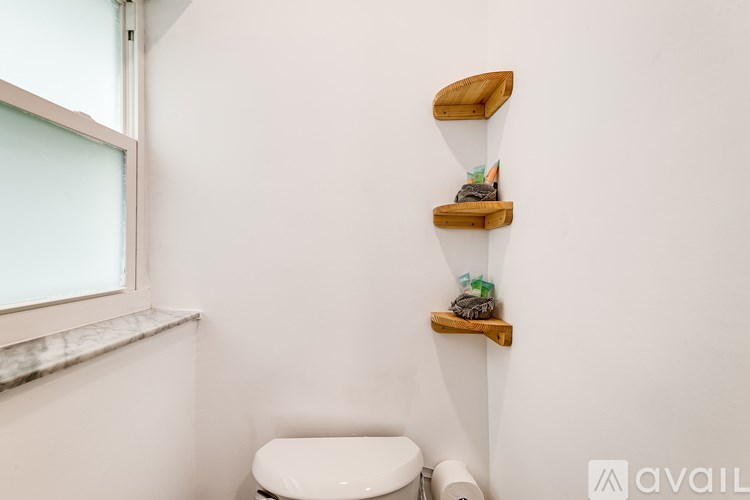 A white toilet sits under a window in a bathroom with a shelf above it.
