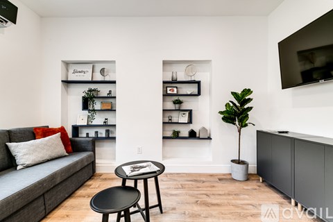 A living room with a grey couch, a black table, and a TV mounted on the wall.