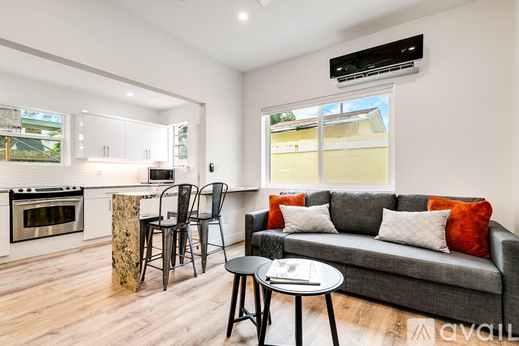 A modern living room with a grey couch, a wooden table, and a kitchen area in the background.