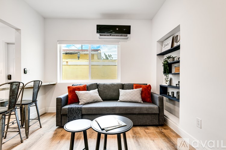 A living room with a grey couch, a black chair, a small table, and a window with a view of the outside.