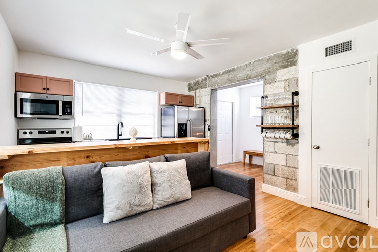 A living room with a grey couch and a kitchen area with a microwave and oven.