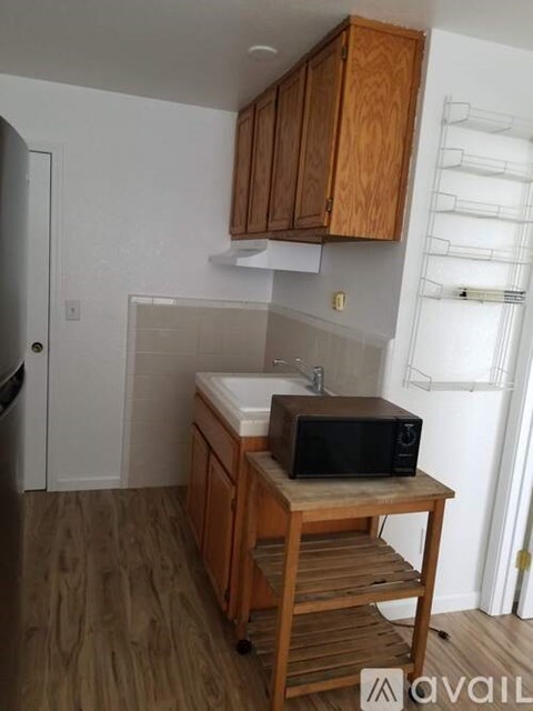 A kitchen with wooden cabinets and a black microwave on a cart.