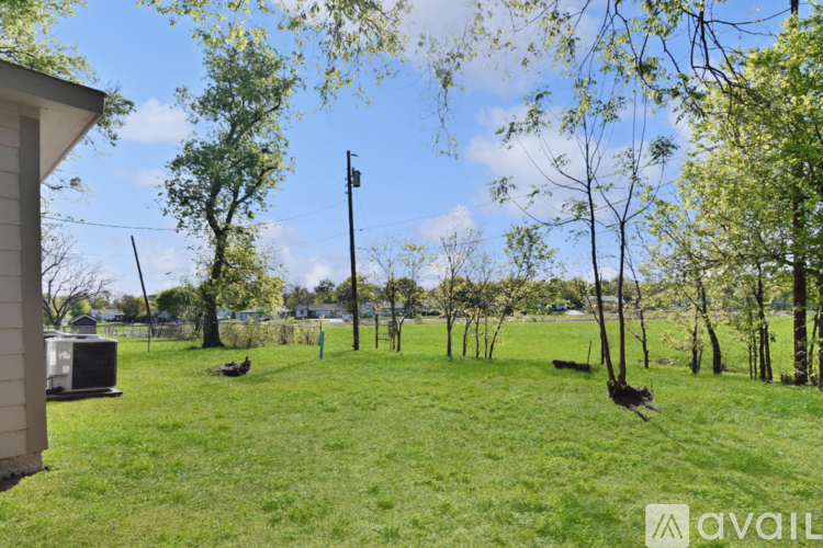 A grassy area with a few trees and a house in the background.