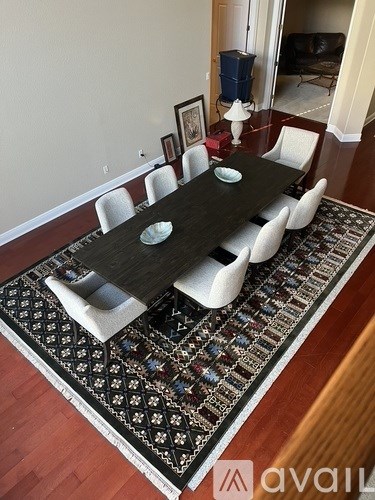 A black table surrounded by white chairs with a patterned rug underneath.