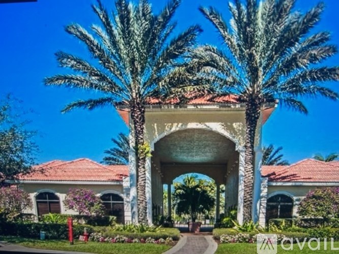 A house with a red roof and a white archway is surrounded by palm trees.