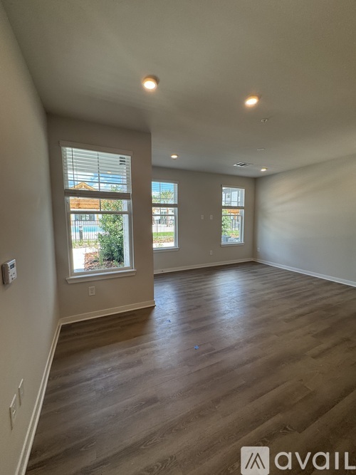 A spacious room with wooden floors and two windows.