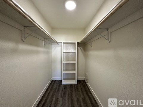 A white ladder is in the middle of a hallway with white walls and dark wood floors.
