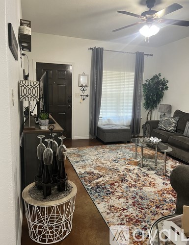 A living room with a rug, a fan, a couch, and a table.