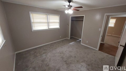 A room with a carpeted floor, a ceiling fan, and a door leading to another room.
