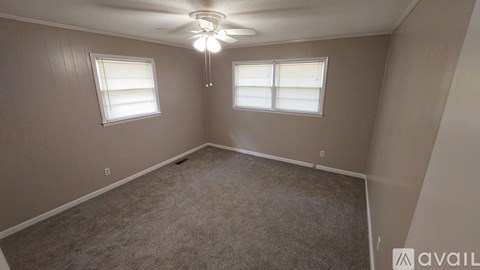A room with a carpeted floor, a ceiling fan, and two windows.