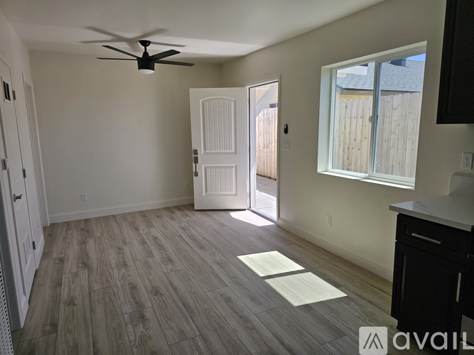 A room with a ceiling fan and light, hardwood floors, and a white door.