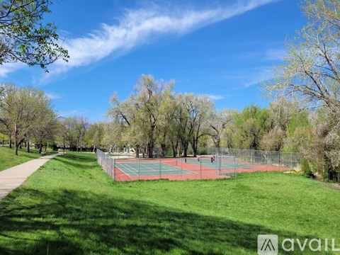 A tennis court is surrounded by a green fence and trees.