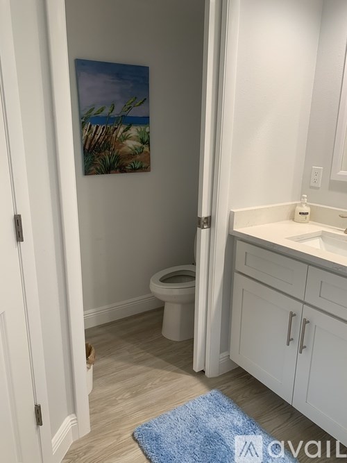A bathroom with a toilet, sink, and a painting of a beach scene on the wall.