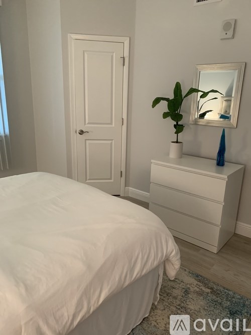 A white bedroom with a bed, dresser, and mirror.