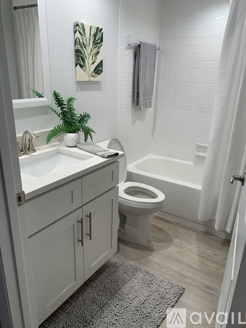 A white bathroom with a toilet, sink, and a plant.