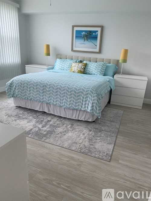 A bed with a blue and white patterned comforter is in the center of a bedroom with a white headboard and two lamps on either side of the bed.