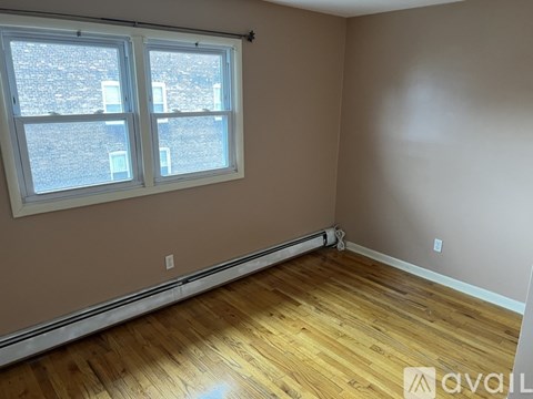A room with wooden flooring and a window overlooking a brick building.