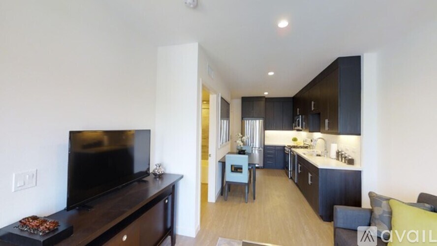 A modern living room with a television and a kitchen area in the background.