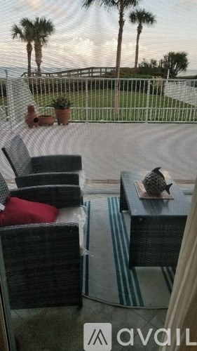 A patio with a table and chairs overlooking a fence and palm trees.