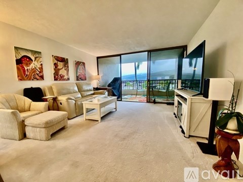 A living room with a white sofa set, a television, and a large window overlooking the beach.