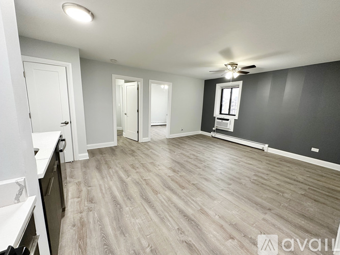 A spacious room with a ceiling fan and light, and a kitchen area with white cabinets and a countertop.
