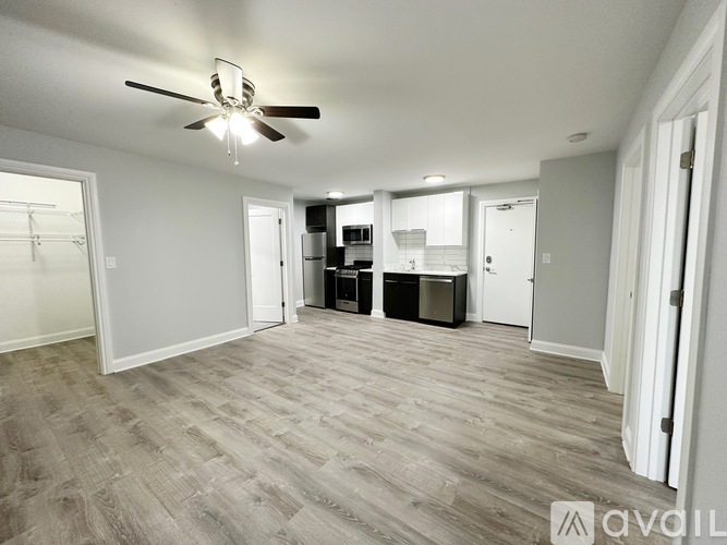 A spacious room with a ceiling fan and lighting fixture, featuring a kitchenette with a refrigerator, microwave, and oven.